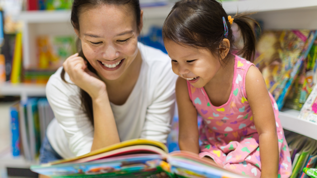 Mother and daughter smiling together while looking through a colorful picture book in a bookstore.