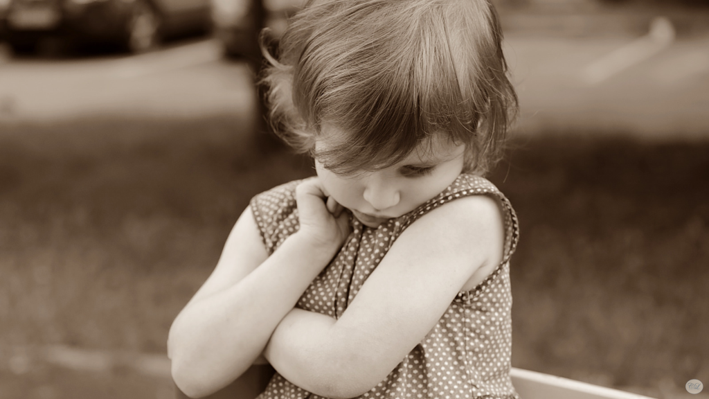 A young child looking down shyly with her arms folded, illustrating feelings of shyness.