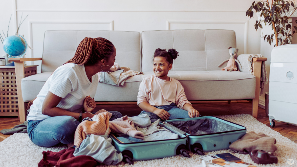 Mother and daughter packing clothes into an open suitcase together at home before a family trip.