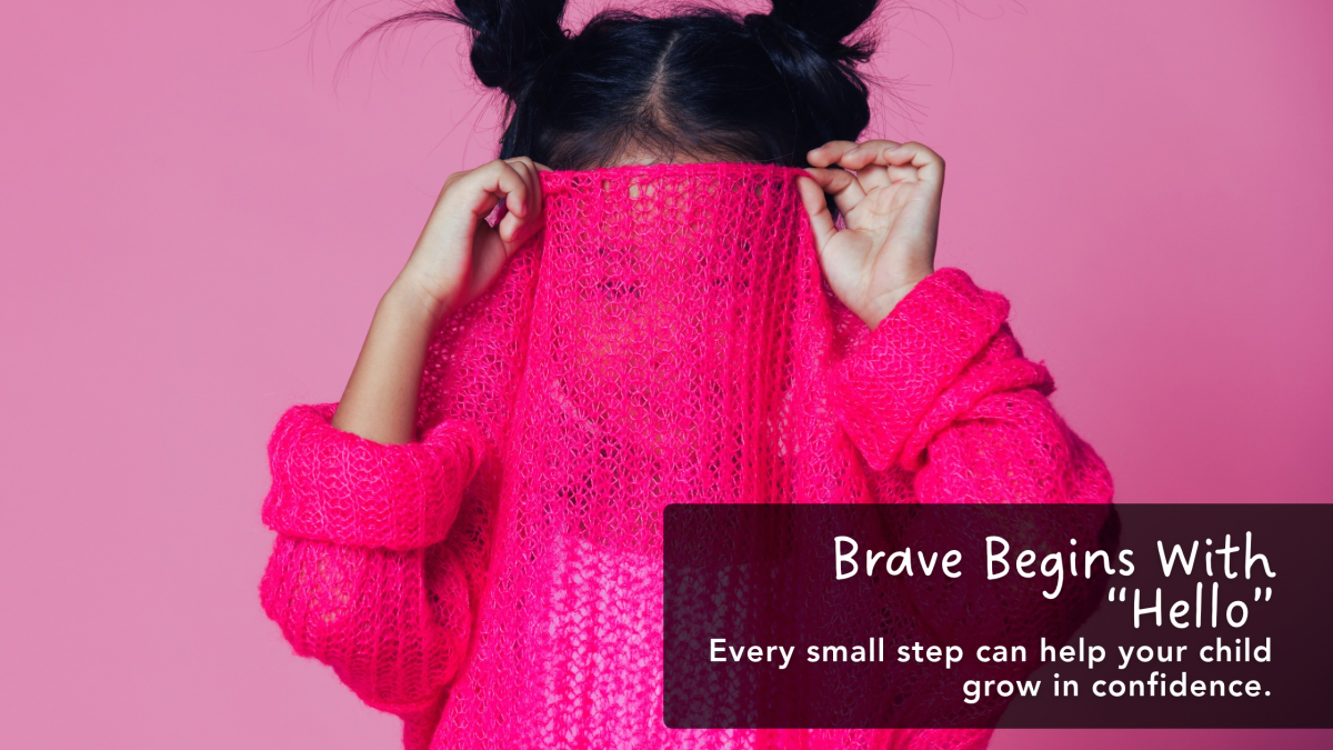A shy child hiding her face behind a bright pink sweater, illustrating the journey toward confidence.